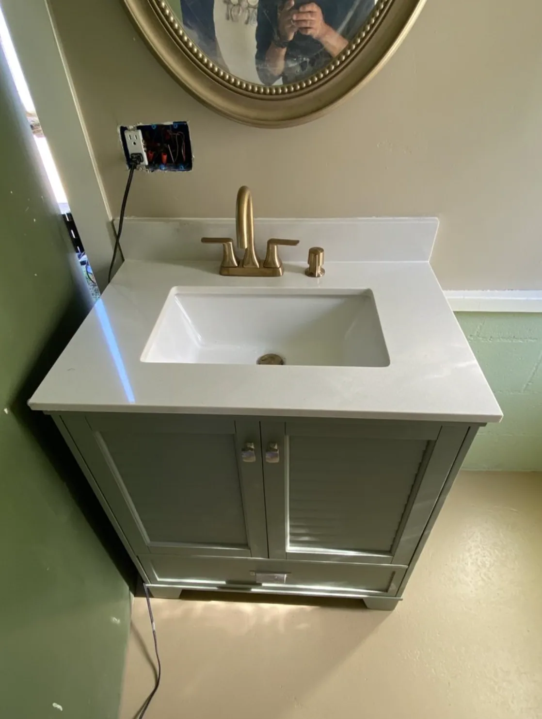 Green bathroom vanity with a white sink and brass faucet during an update
