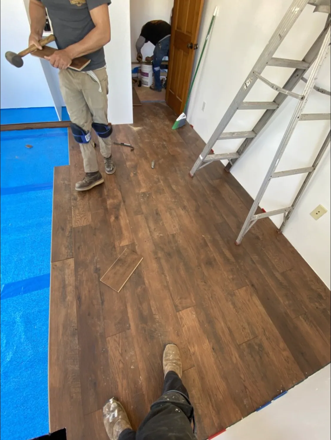 Workers installing wood-look floor planks over blue underlayment