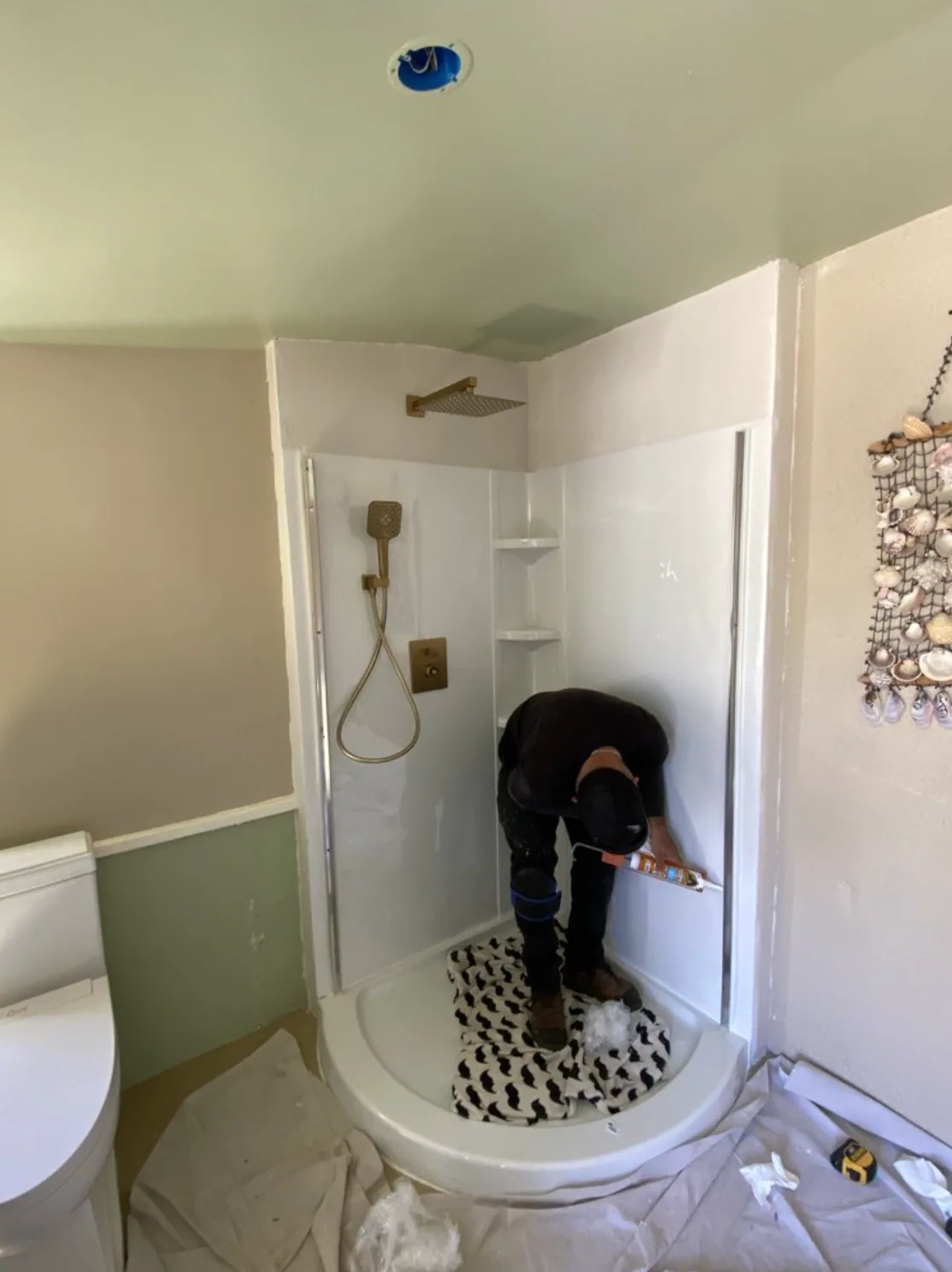 Worker finishing a white shower surround with brass shower fixtures